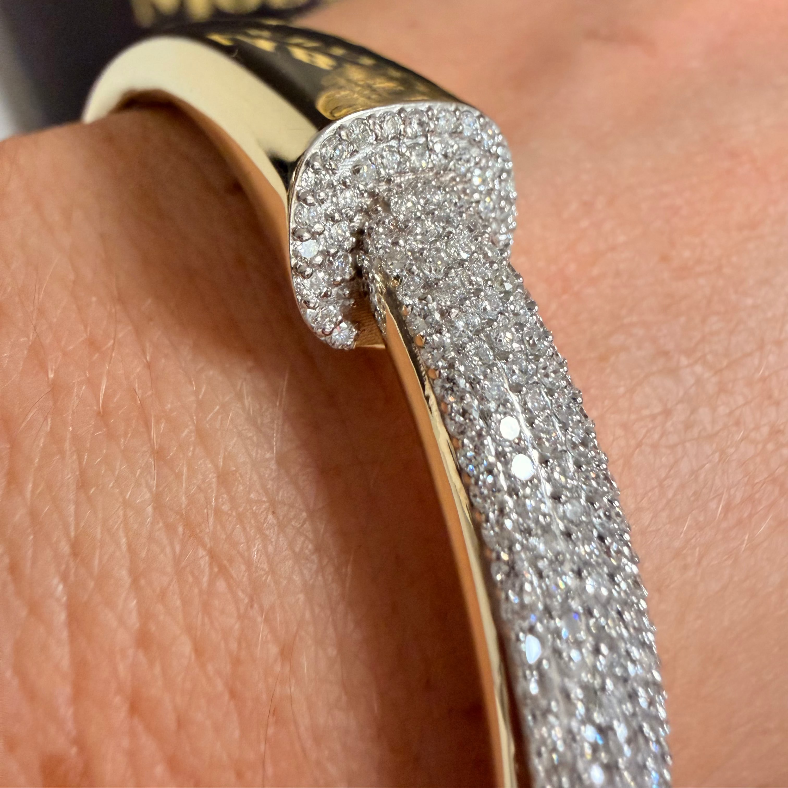 A close-up of a gold bangle bracelet with a pavé-set diamond arrowhead detail, worn on a person's wrist.