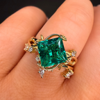 Gold ring with a green gemstone on a hand against a dark background