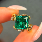 Gold ring with a large green gemstone held between fingers against a neutral background