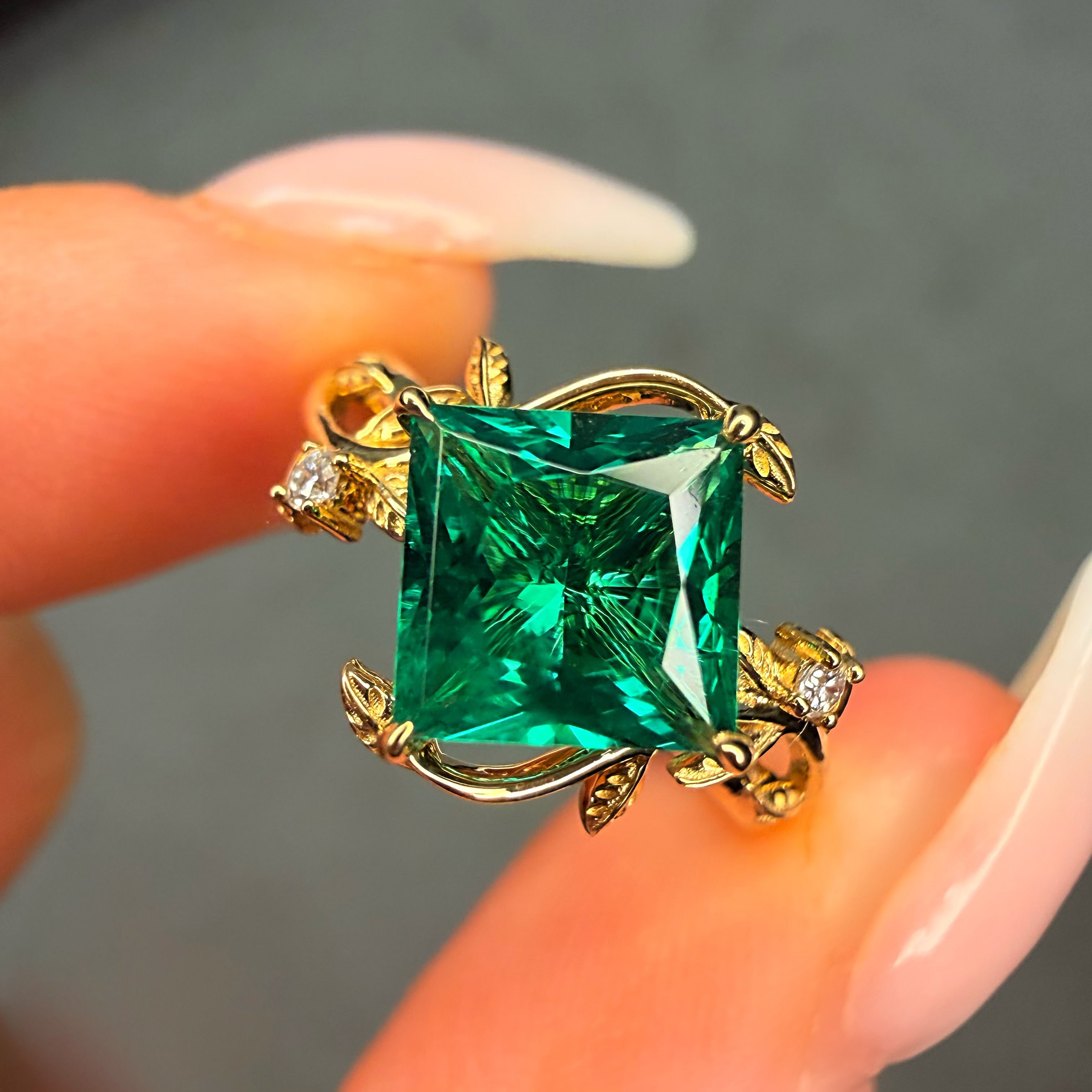 Gold ring with a large green gemstone held between fingers against a neutral background