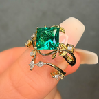Gold ring with a large green gemstone held on a finger against a neutral background