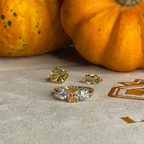 Gold and diamond ring with two diamonds on a textured surface next to pumpkins.