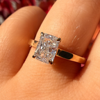 A close-up of a yellow gold ring with a rectangular radiant-cut diamond set on a finger.