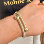 A close-up of a person's wrist wearing two gold-toned bangle bracelets, with a dark sign reading 'Ireland's Mobile Jewellery' in the background.