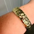 Gold textured bracelet on a wrist with a white paneled background