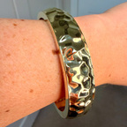 Gold textured bracelet on a wrist with a neutral background