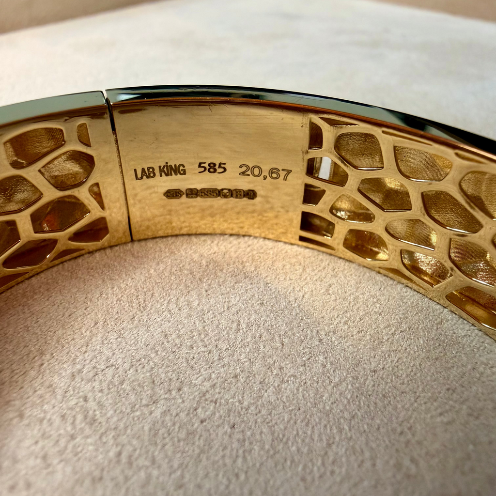 Gold bracelet with intricate design on a beige cushion