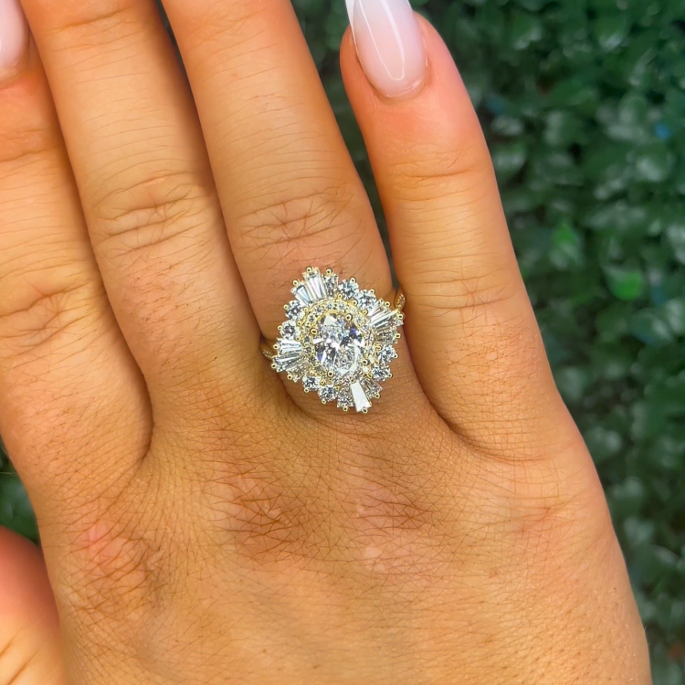 Hand wearing a gold ring with a large diamond on a green grass background