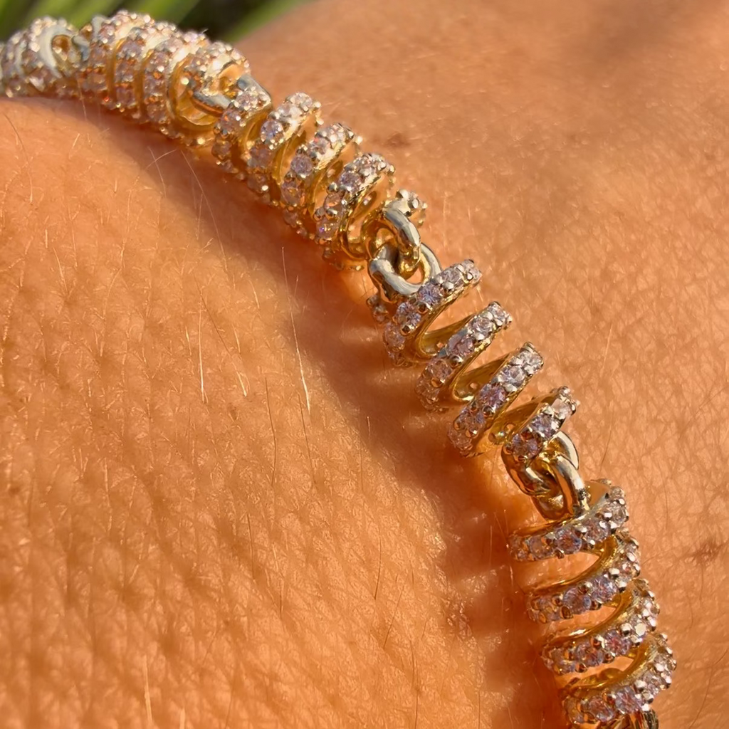 Gold bracelet with diamonds on a person's wrist against a blurred natural background