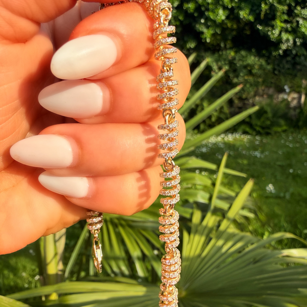 Hand holding a gold bracelet with green foliage in the background