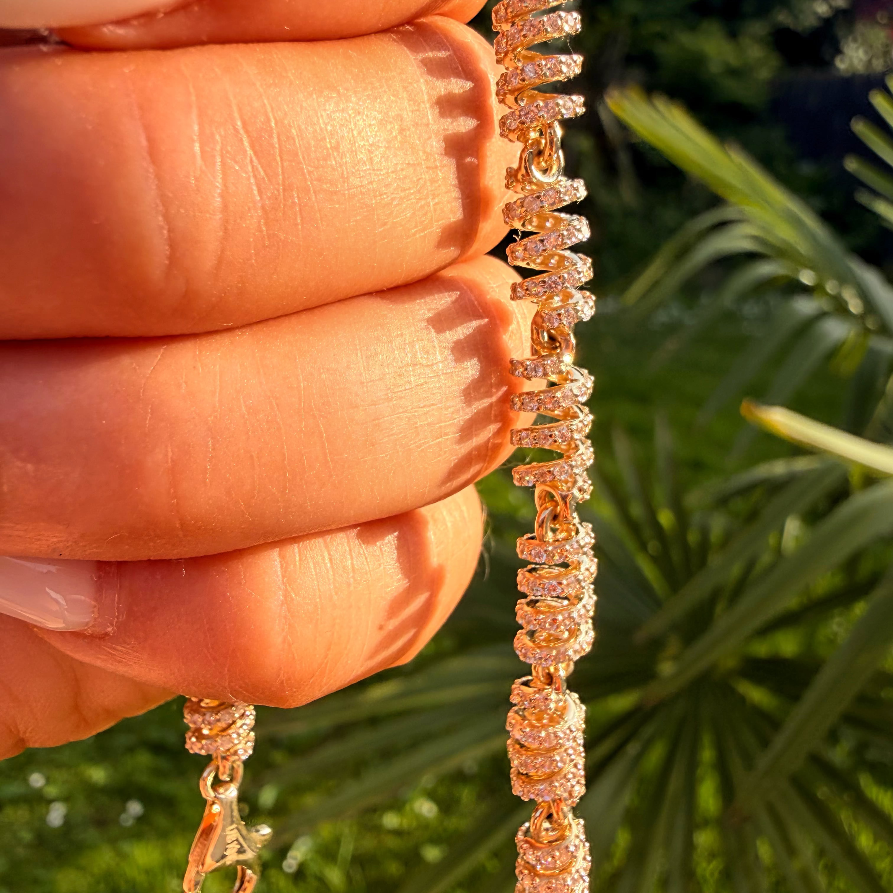 Rose gold bracelet held between fingers with a blurred green outdoor background
