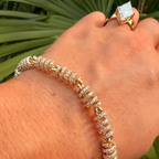 Hand wearing a gold and diamond bracelet with a matching ring against a green leafy background