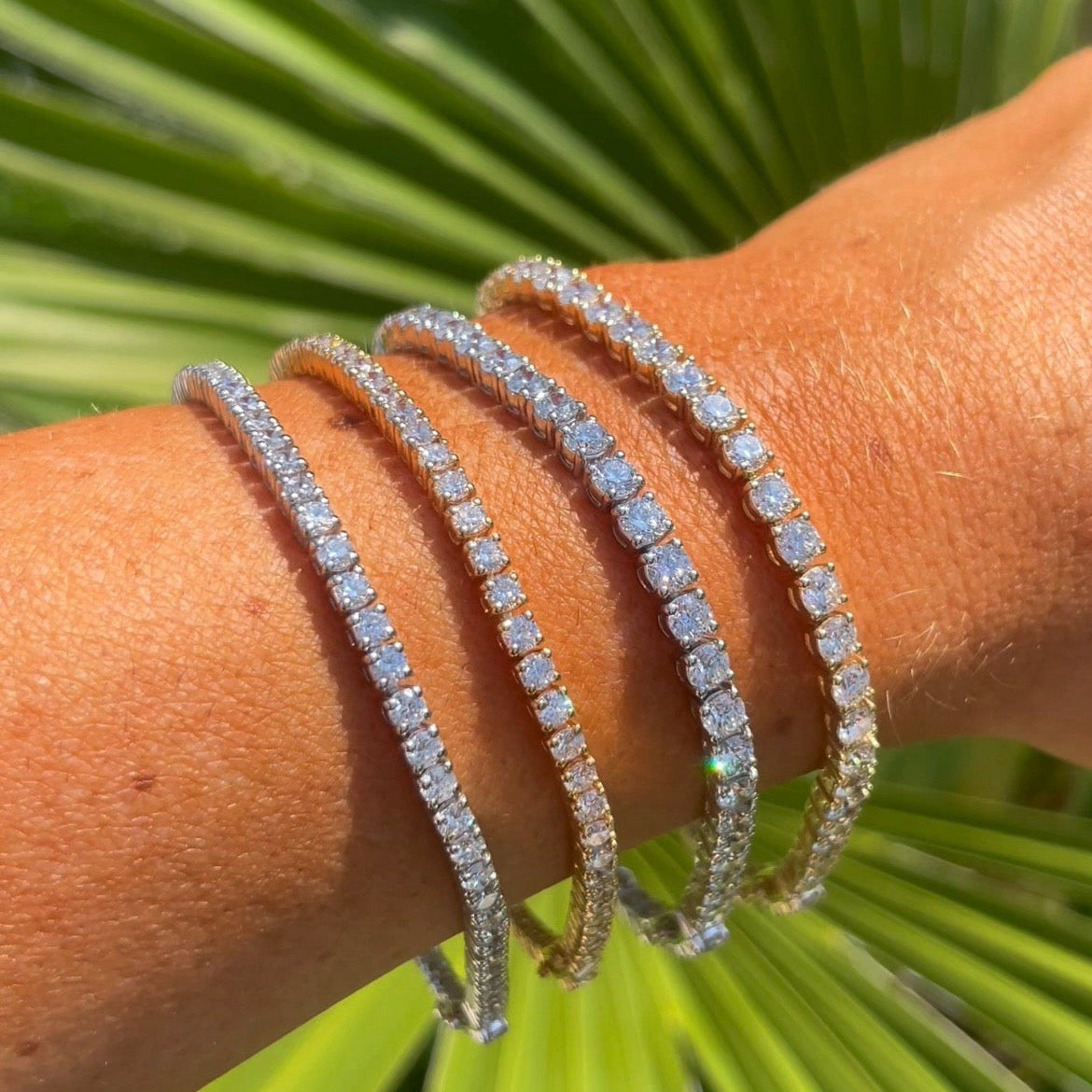 Close-up of a wrist wearing multiple diamond bracelets with a green leafy background