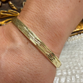 A close-up of a textured gold bangle bracelet worn on a person's wrist.
