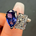 Two gemstones, one blue and one clear, held between fingers against a dark background.