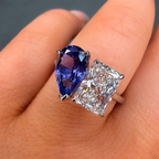 Ring with blue gemstone and diamond on a finger against a neutral background