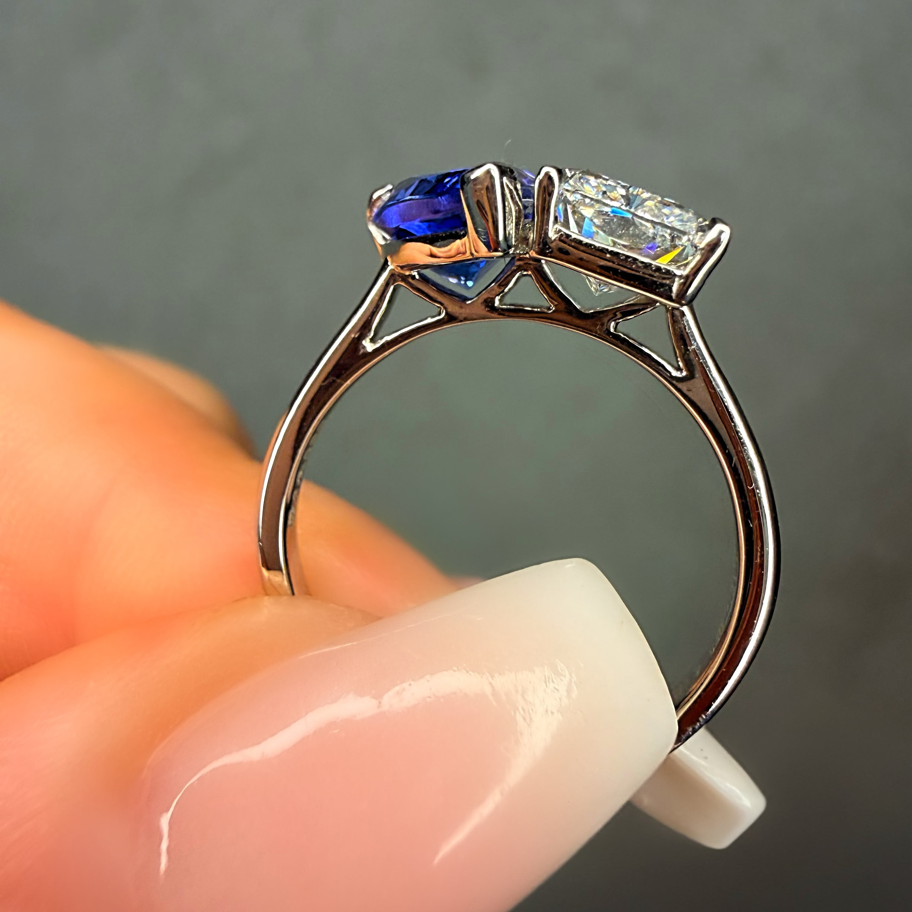 Ring with blue gemstone and clear diamond held by a hand against a gray background