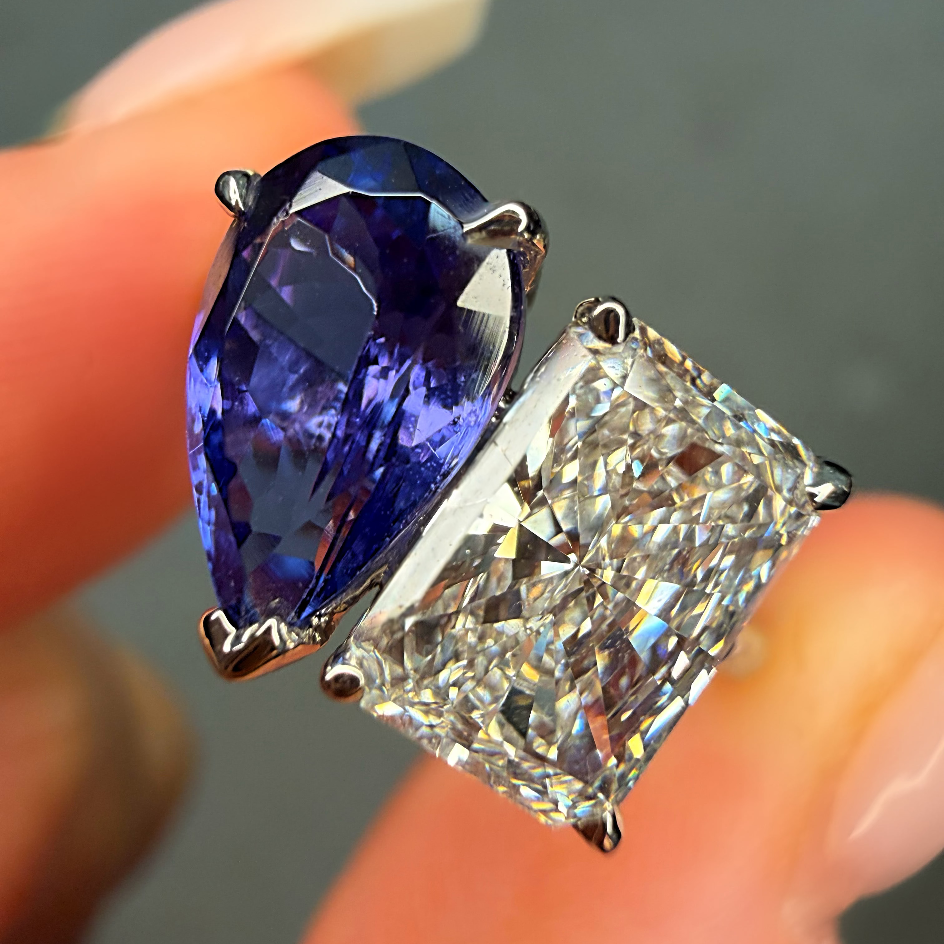 Close-up of a blue gemstone and diamond ring held between fingers.