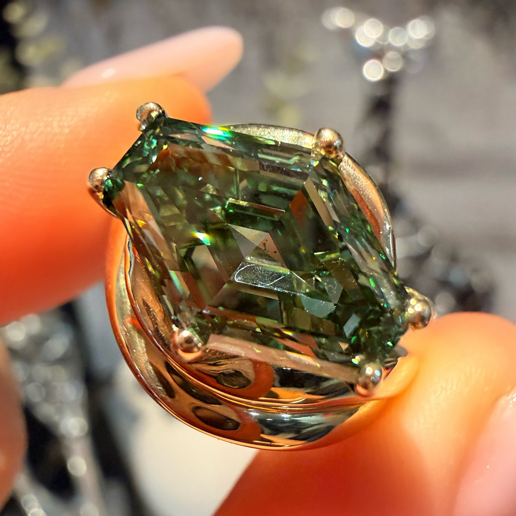 A close-up of a gold ring with a marquise-cut green gemstone being held between fingers.