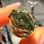 A close-up of a gold ring with a marquise-cut green gemstone being held between fingers.