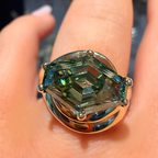 A close-up of a hand wearing a large ring with a faceted green gemstone in a gold-toned setting.