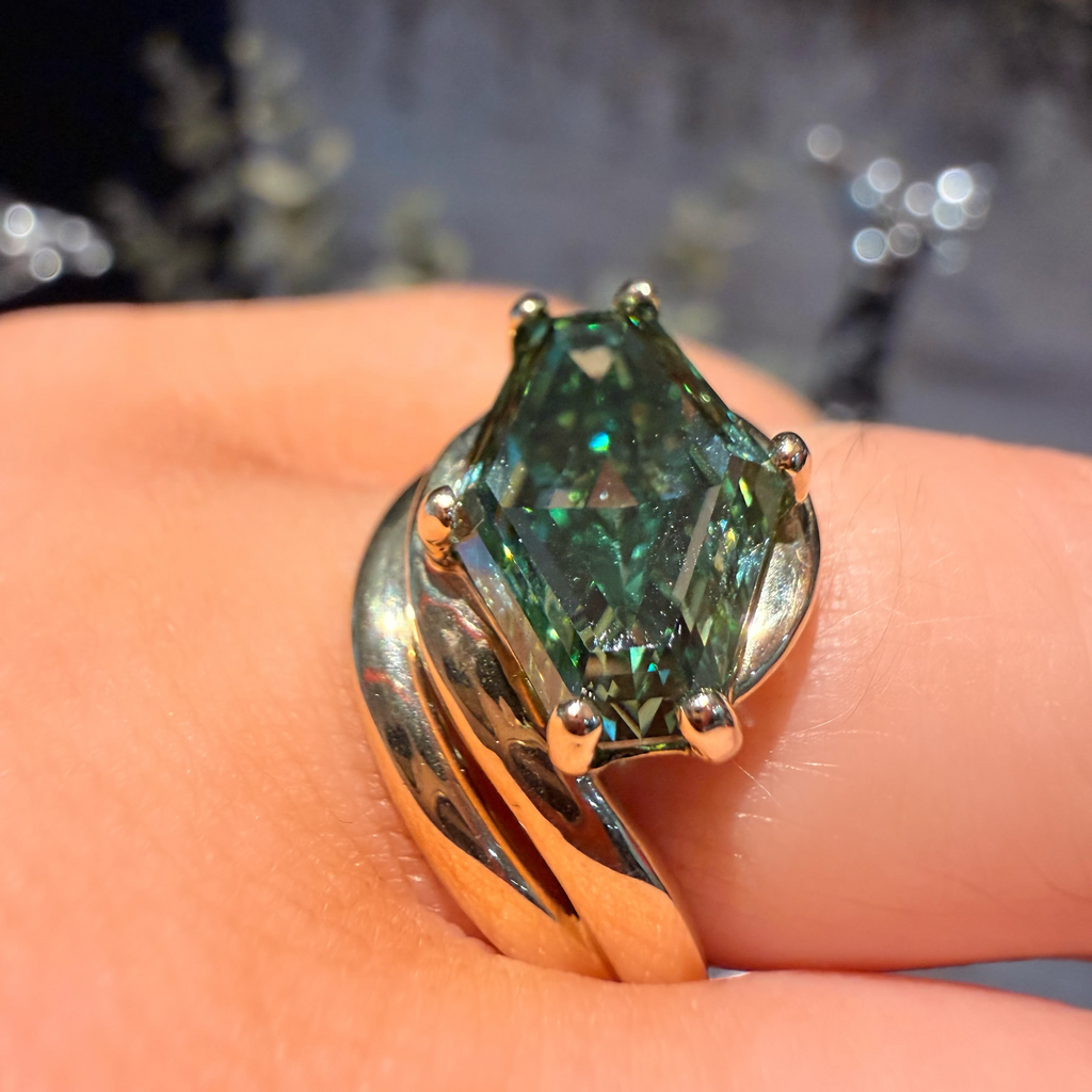 A close-up of a gold ring with a marquise-cut green gemstone worn on a finger.