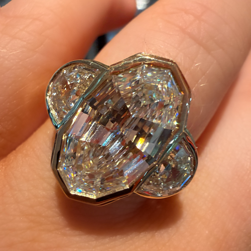 A close-up of a large, multi-faceted clear gemstone ring with a gold-toned setting, worn on a person's finger.