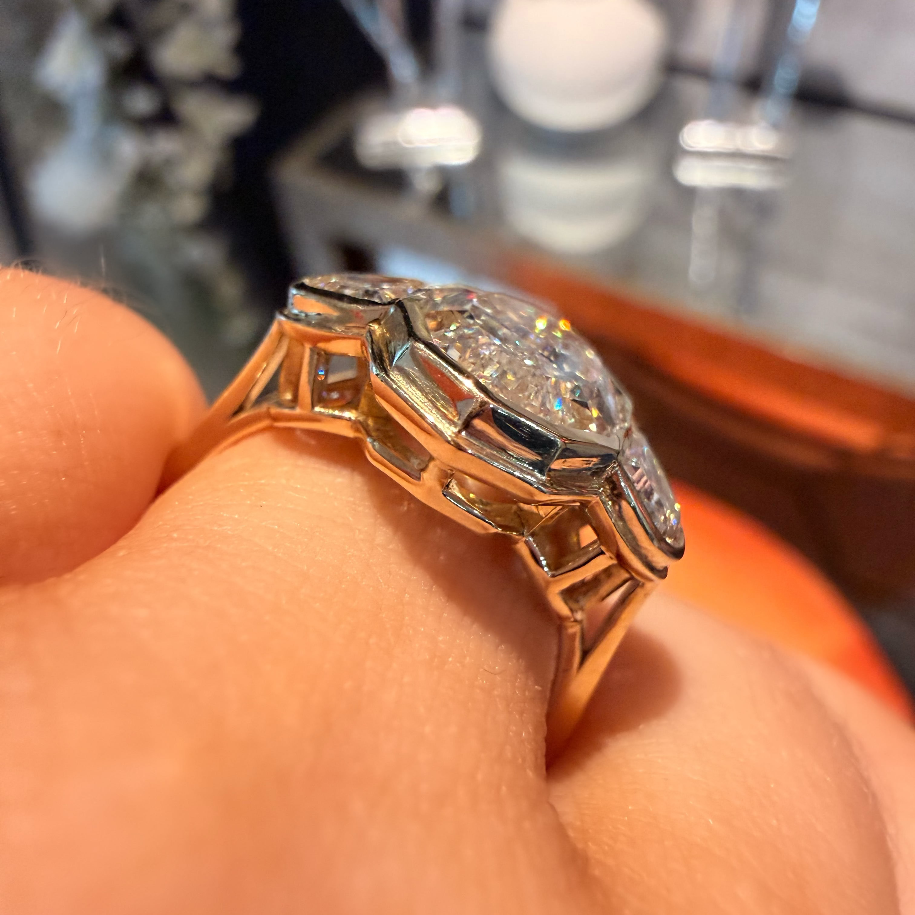 A close-up shot of a vintage-style Art Deco ring being worn on a finger. The ring features a large clear gemstone in a geometric setting with a warm gold-toned band and dark inlay details.