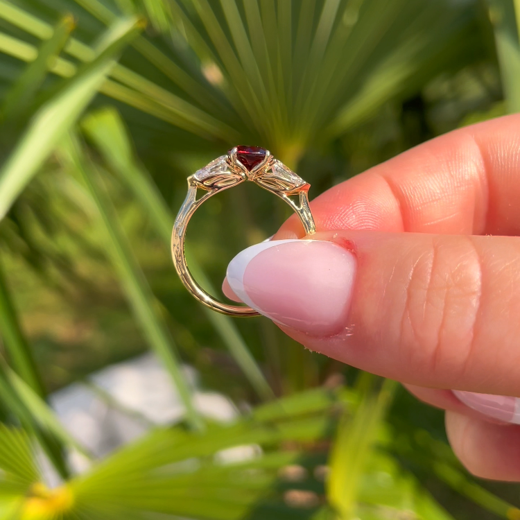 Ring with a red gemstone held by a hand against a green leafy background
