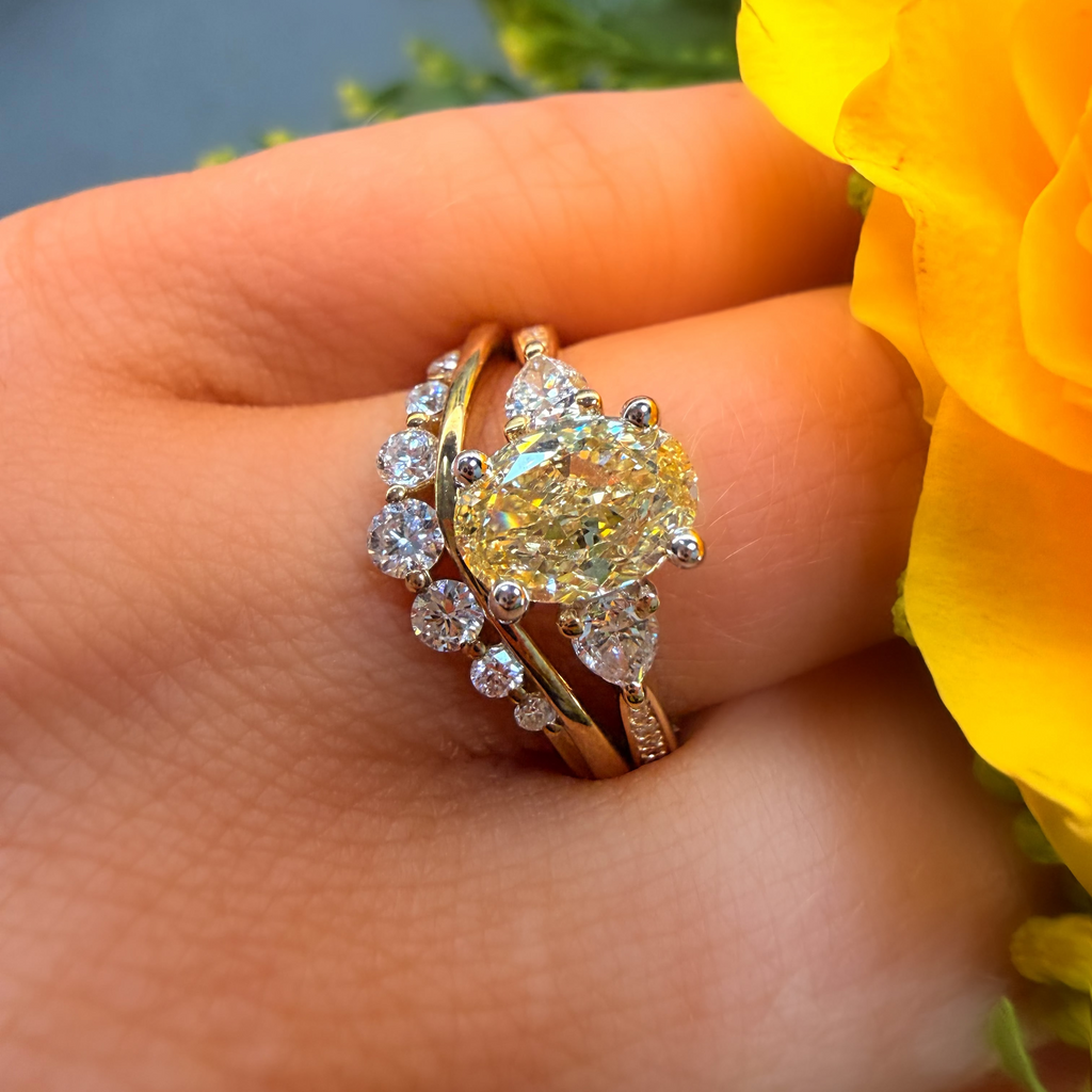 Gold ring with a large yellow gemstone on a hand with a yellow flower in the background
