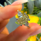Gold ring with large yellow gemstone held by a hand against a blurred natural background