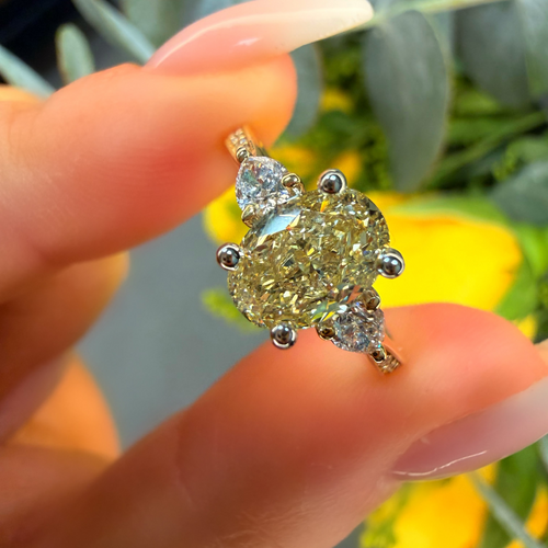 Gold ring with large yellow gemstone held by a hand against a blurred natural background