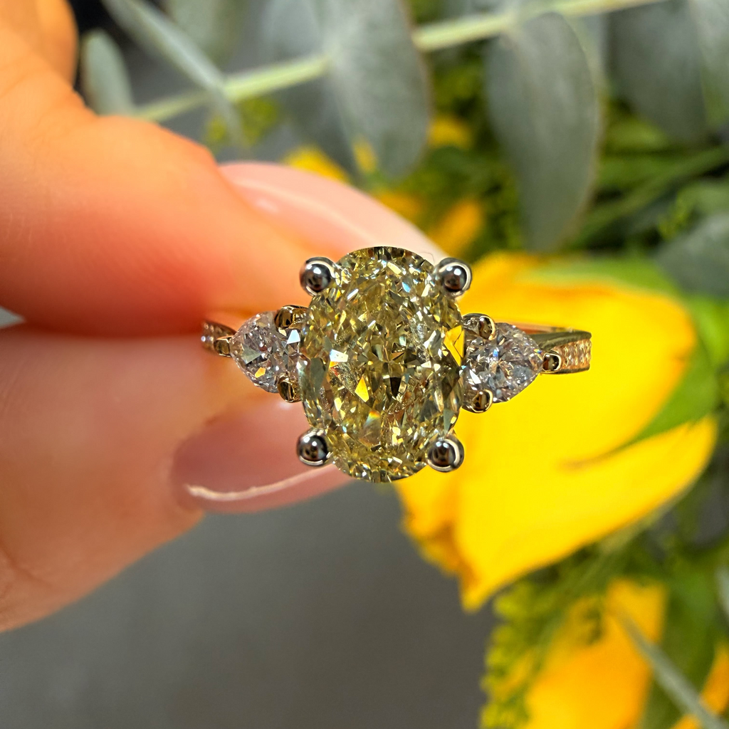 Gold ring with a large yellow gemstone held by a hand against a blurred floral background