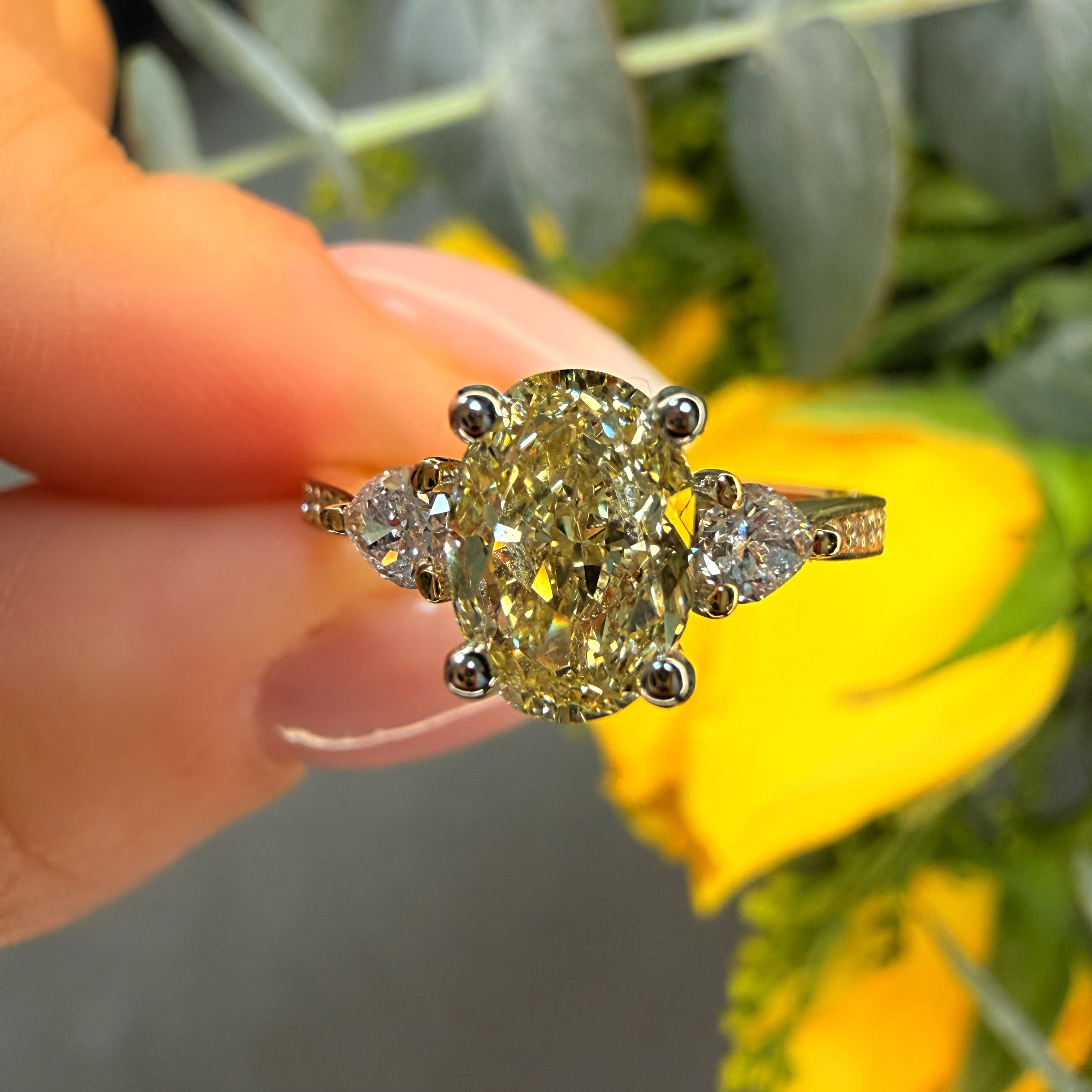 Gold ring with a large yellow gemstone held by a hand against a blurred floral background