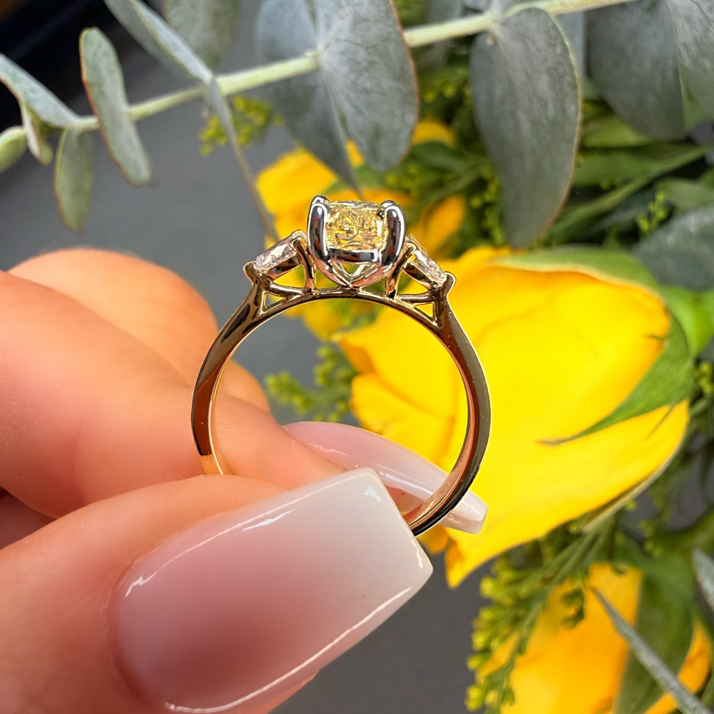 Gold ring with a yellow gemstone held by a hand against a floral background