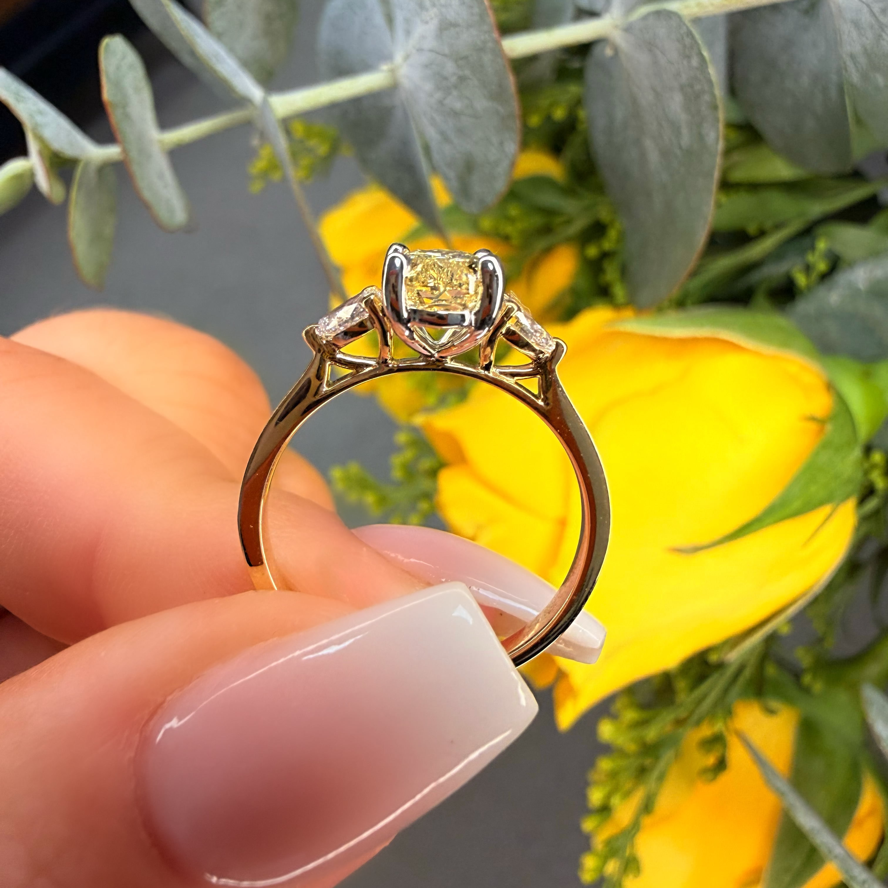 Gold ring with a yellow gemstone held by a hand against a floral background