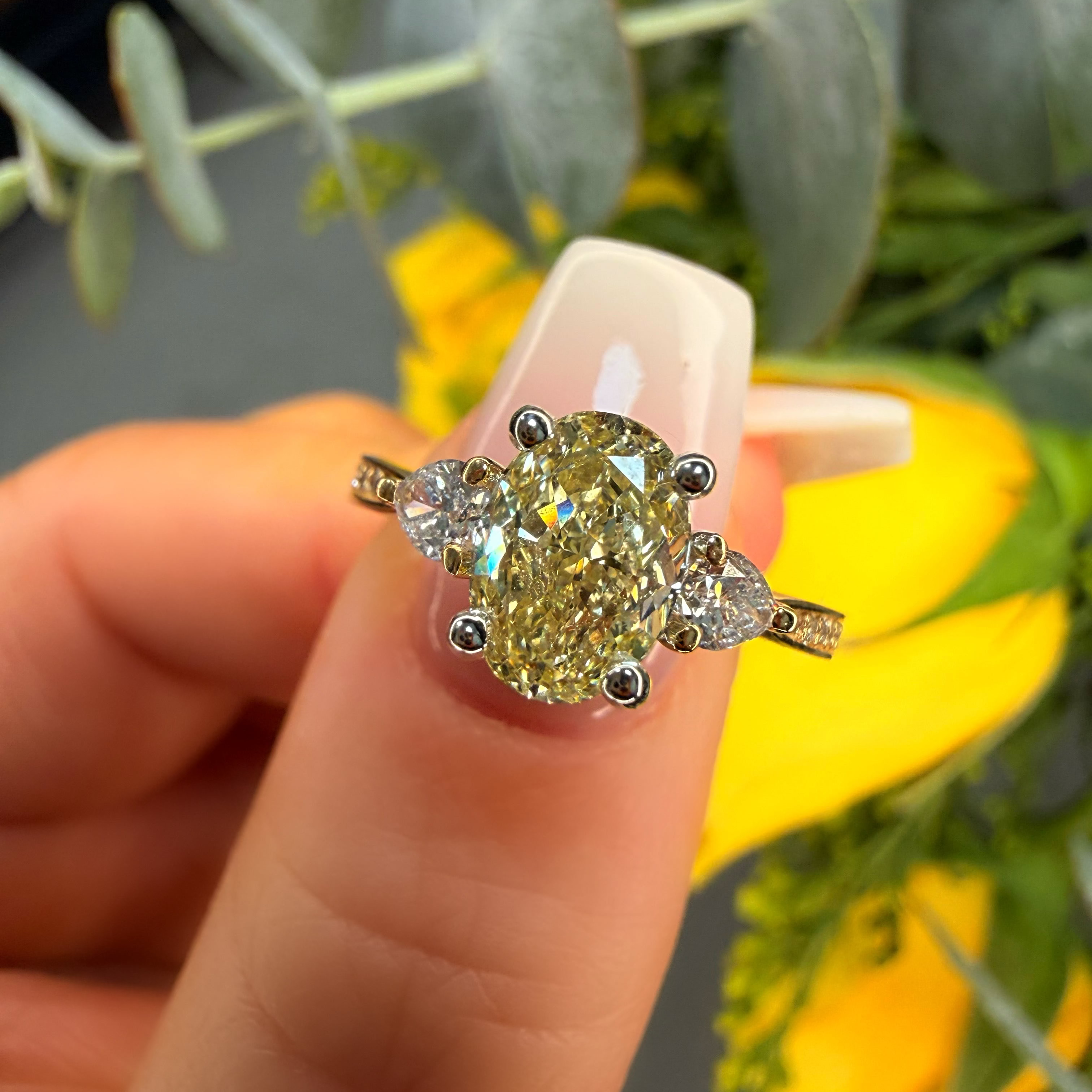 Diamond ring held between fingers with a blurred floral background