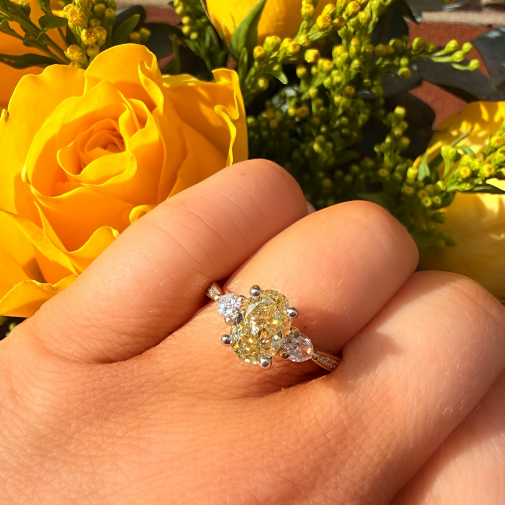 Gold ring with a yellow gemstone on a hand with yellow flowers in the background